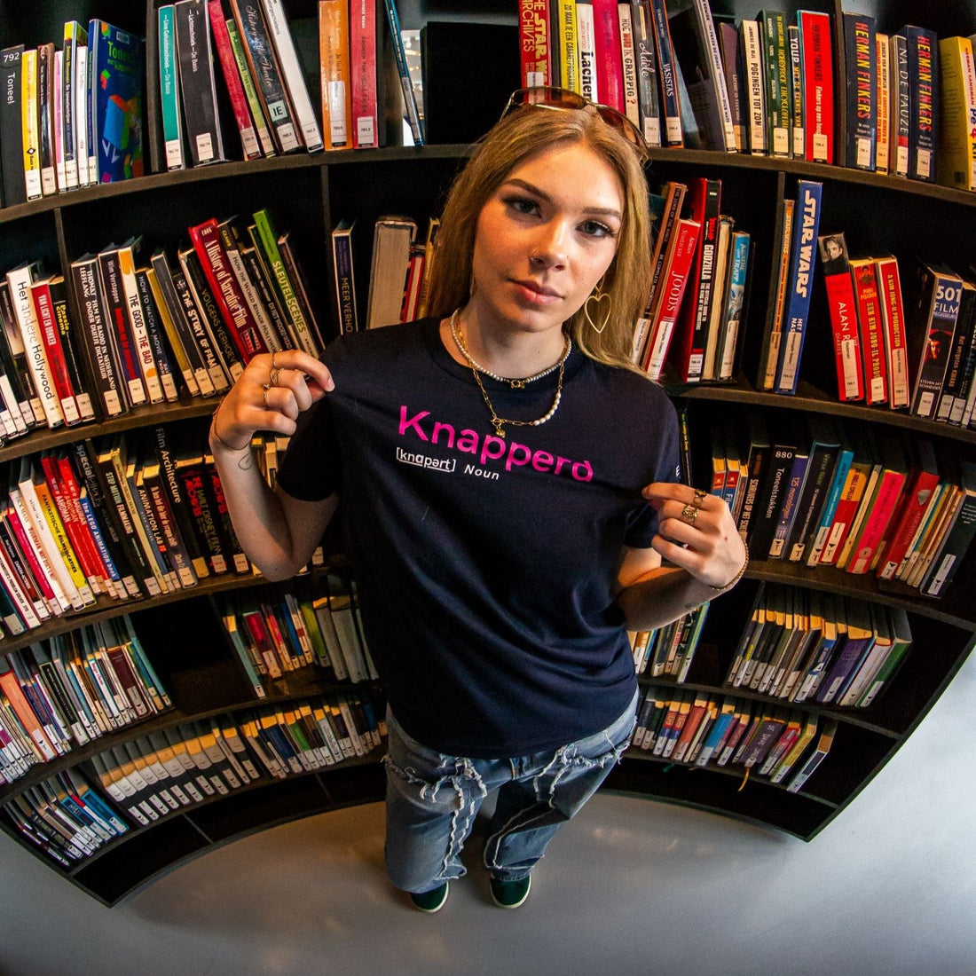picture with fish-eye effect of a woman wearing a dark blue t-shirt. Print on the t-shirt reads "Knapperd".