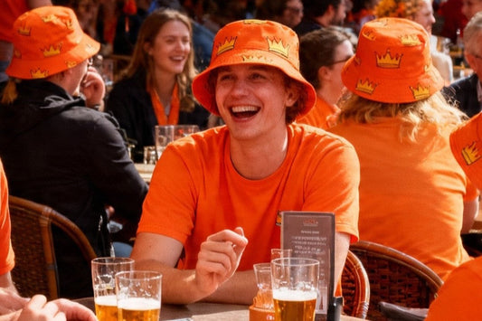 Man in orange laughing wearing orange bucket hat covered in yellow crown pattern.